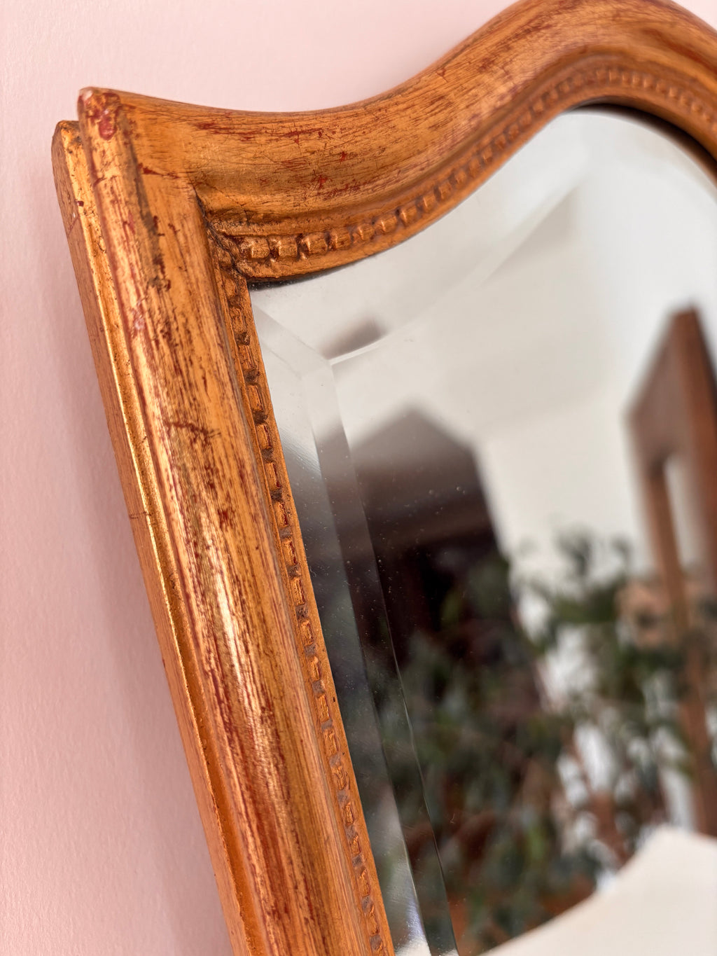 Close-up of the arched top of a vintage gold framed wall mirror showing worn patina