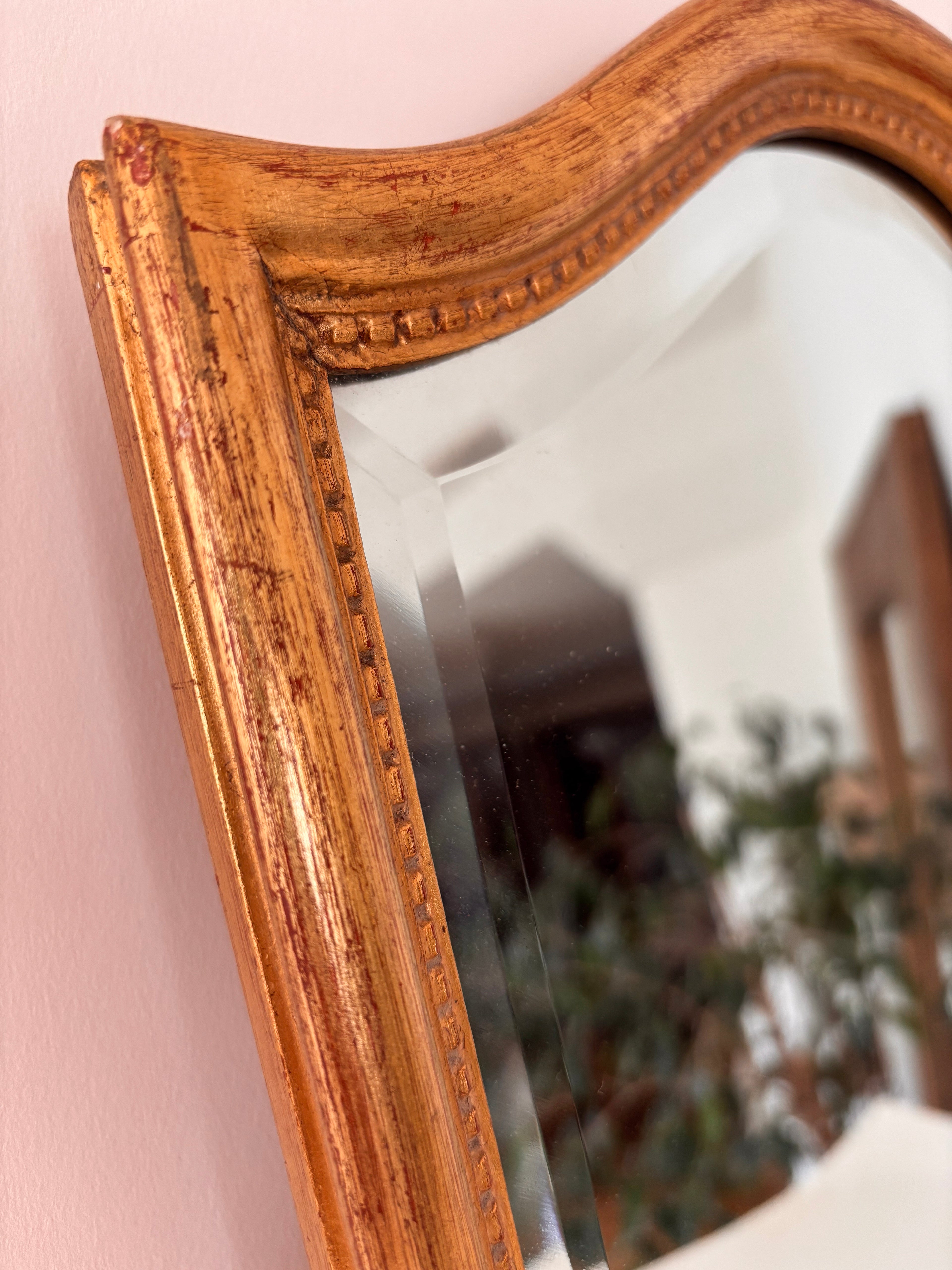 Close-up of the arched top of a vintage gold framed wall mirror showing worn patina