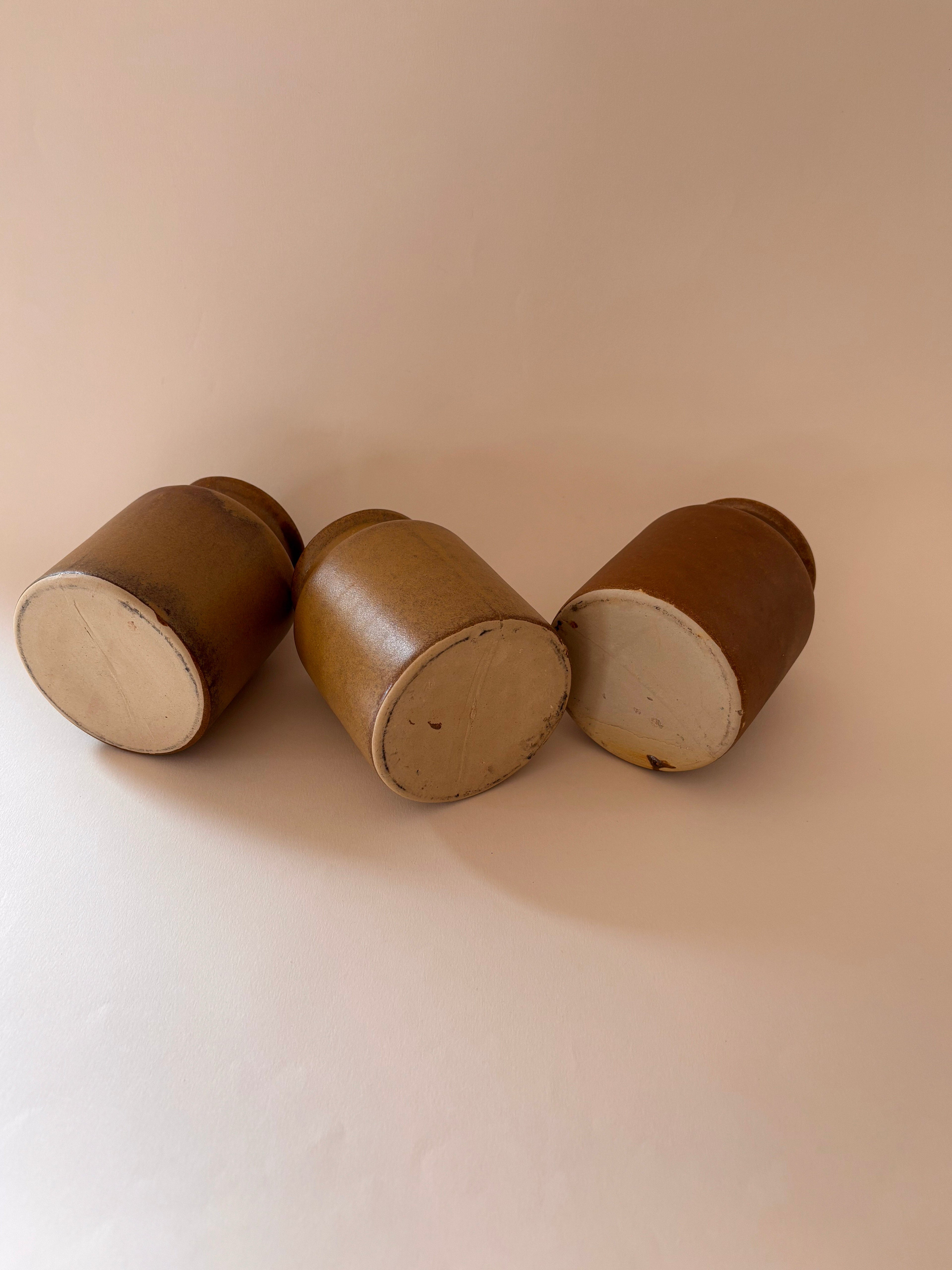 Three vintage French stoneware mustard jars, base view, showing unglazed stoneware foot and natural clay texture.
