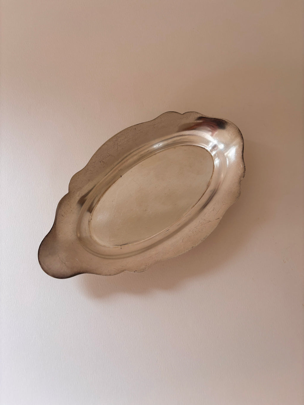 Vintage silver-plated oval dish with scalloped edges and softly luminous surface, seen from above