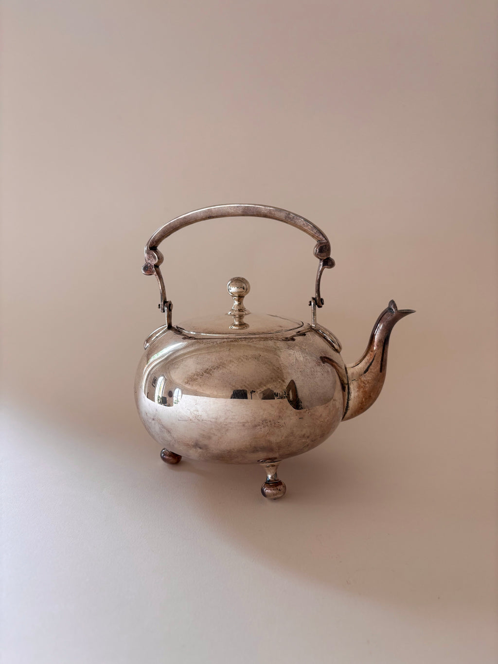 Vintage silver-plated teapot with ball feet, arched handle and finial lid on a neutral background