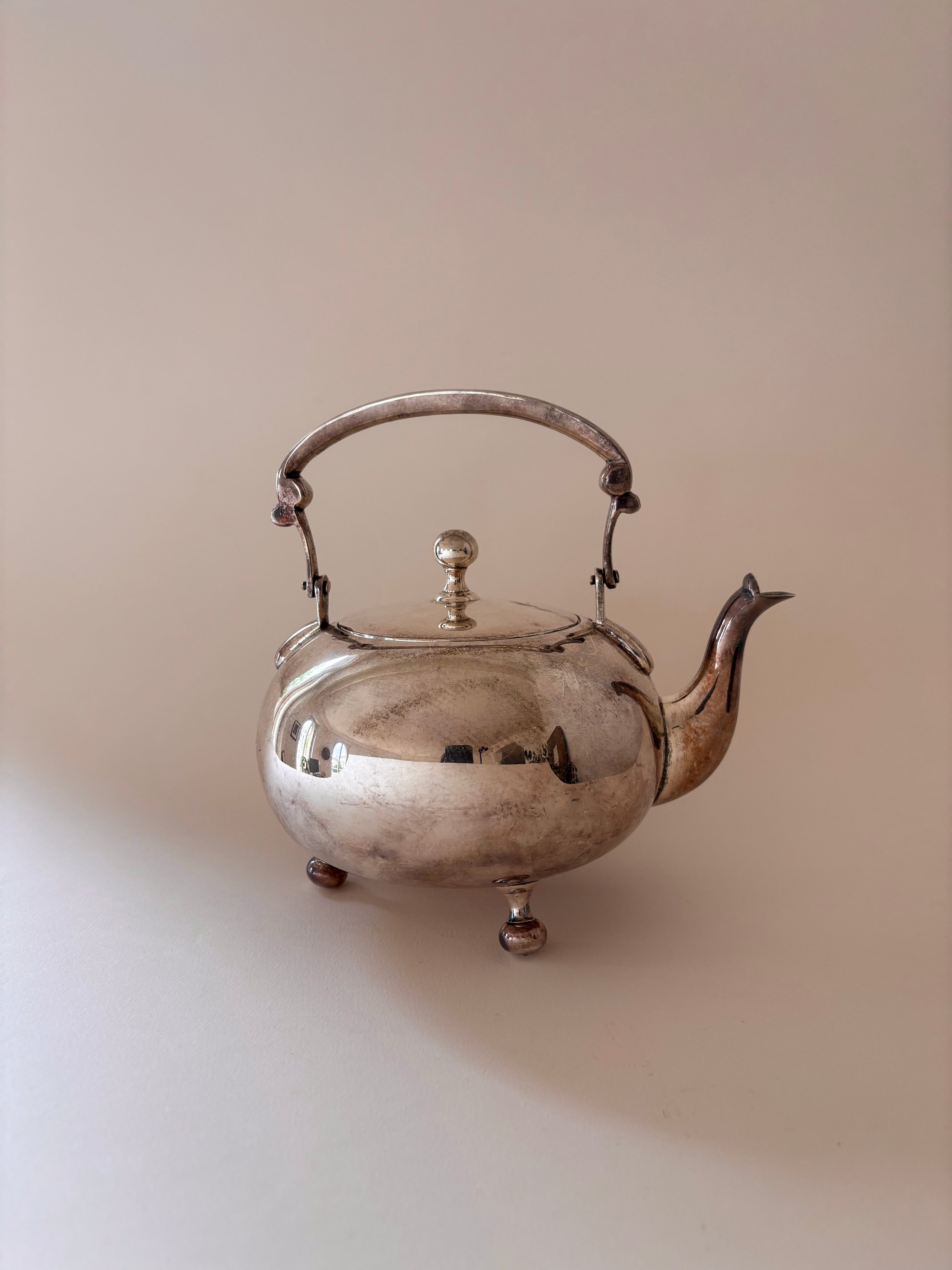Vintage silver-plated teapot with ball feet, arched handle and finial lid on a neutral background