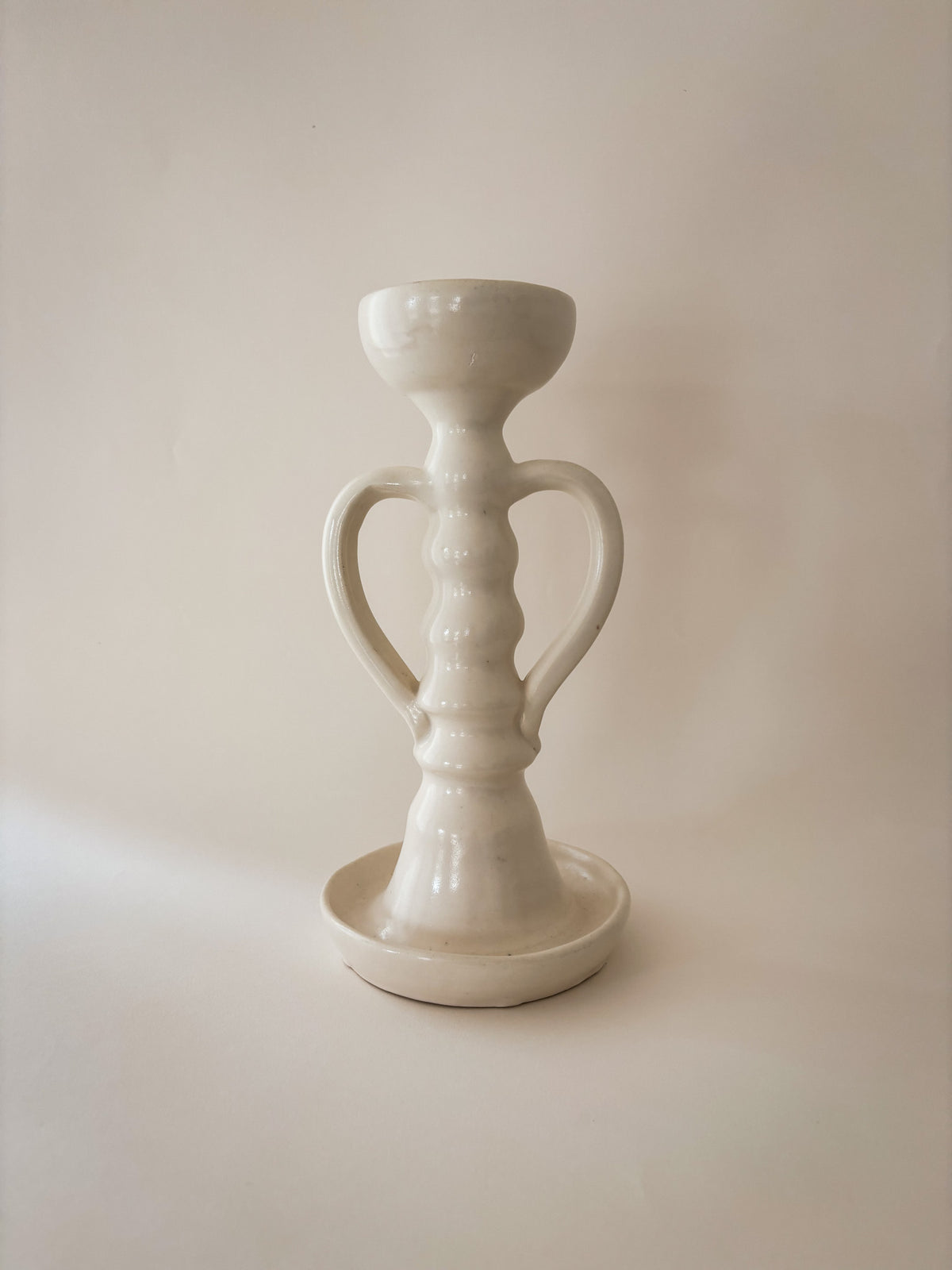 A single white ceramic candle holder holder with two loop handles and a round saucer base