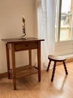 a vintage stool and Wooden side table with a a brass candlestick next to a window with white curtains.