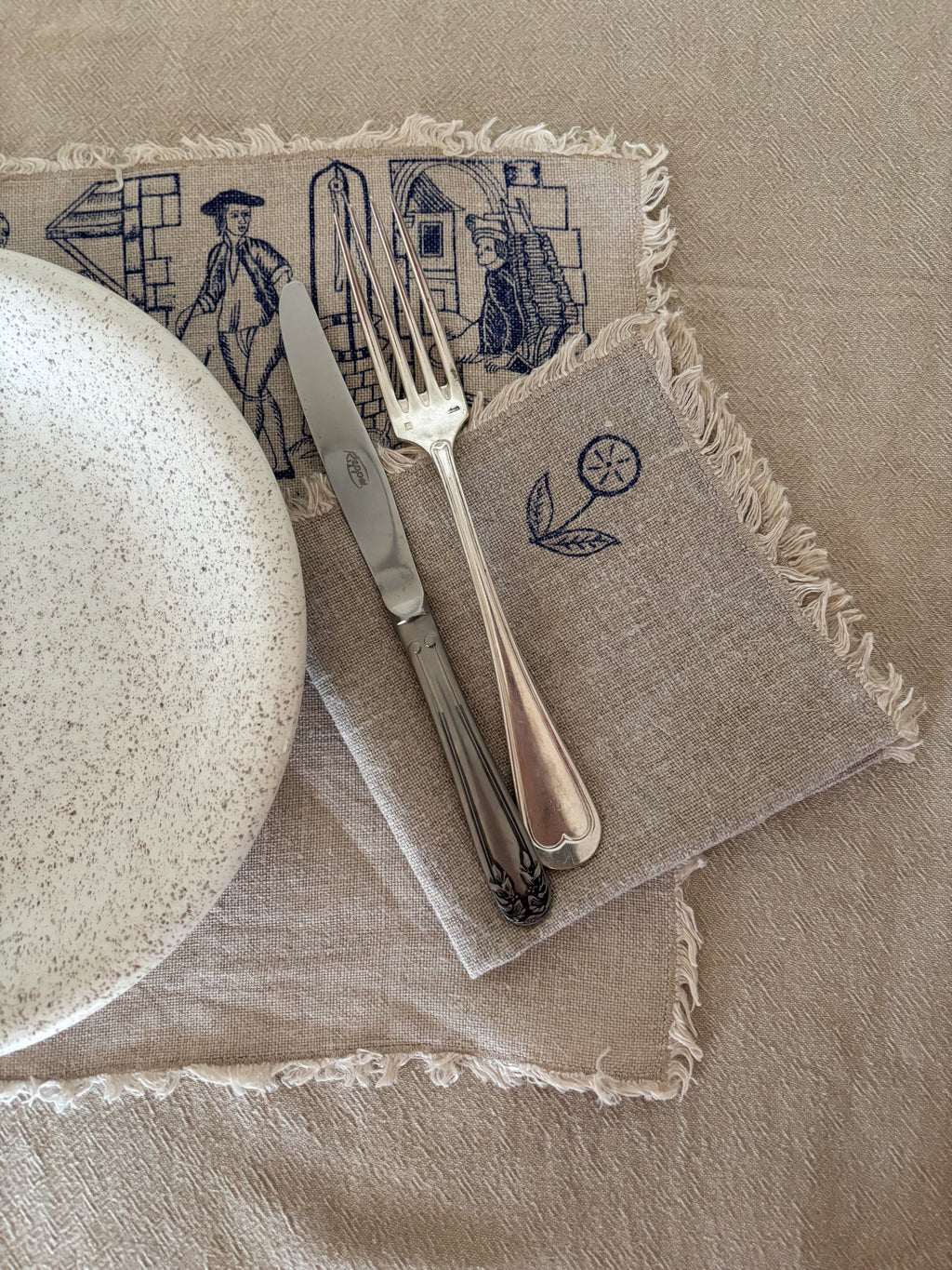 Napkin with embroidered designs featuring a plate, knife, and fork on a beige background