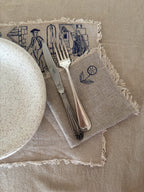 Napkin with embroidered designs featuring a plate, knife, and fork on a beige background