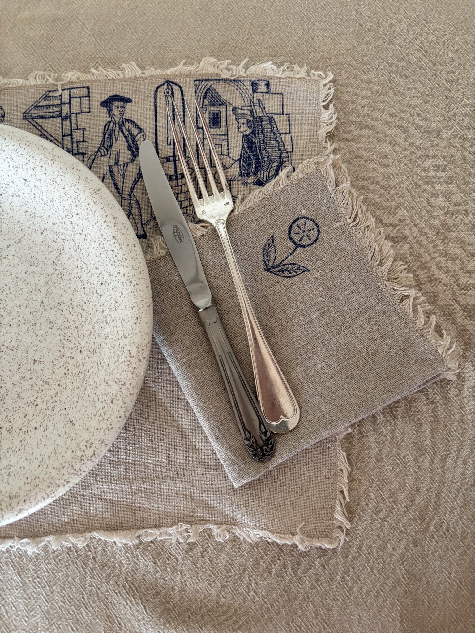 Napkin with embroidered designs featuring a plate, knife, and fork on a beige background
