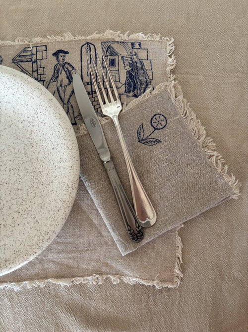 Napkin with embroidered designs featuring a plate, knife, and fork on a beige background